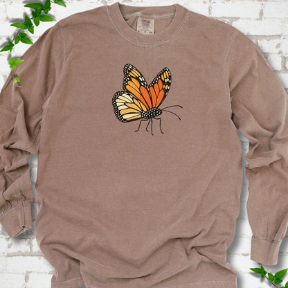 Espresso brown long sleeve T-shirt with one large orange and black monarch butterfly, wings raised, printed on the chest, flat lay on white brick with ivy