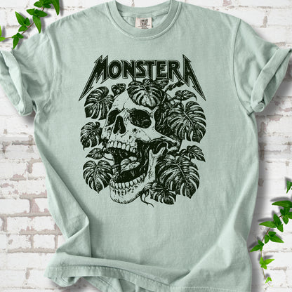 Bay Comfort Colors® T-shirt with distressed skull and monstera leaves beneath MONSTERA lettering, flat lay on white brick.