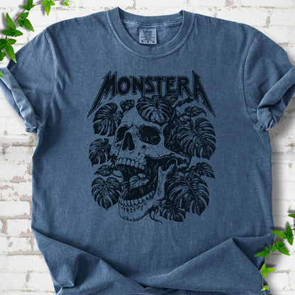 Denim Comfort Colors® T-shirt with distressed skull and monstera leaves beneath MONSTERA lettering, flat lay on white brick.