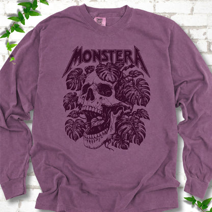 Berry Comfort Colors® long sleeve T-shirt with distressed skull and monstera leaves beneath MONSTERA lettering, flat lay on white brick.