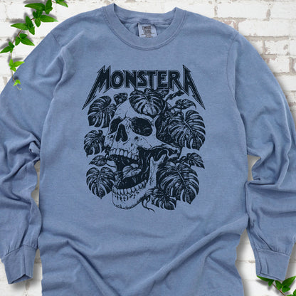 Blue Jean Comfort Colors® long sleeve T-shirt with distressed skull and monstera leaves beneath MONSTERA lettering, flat lay on white brick.