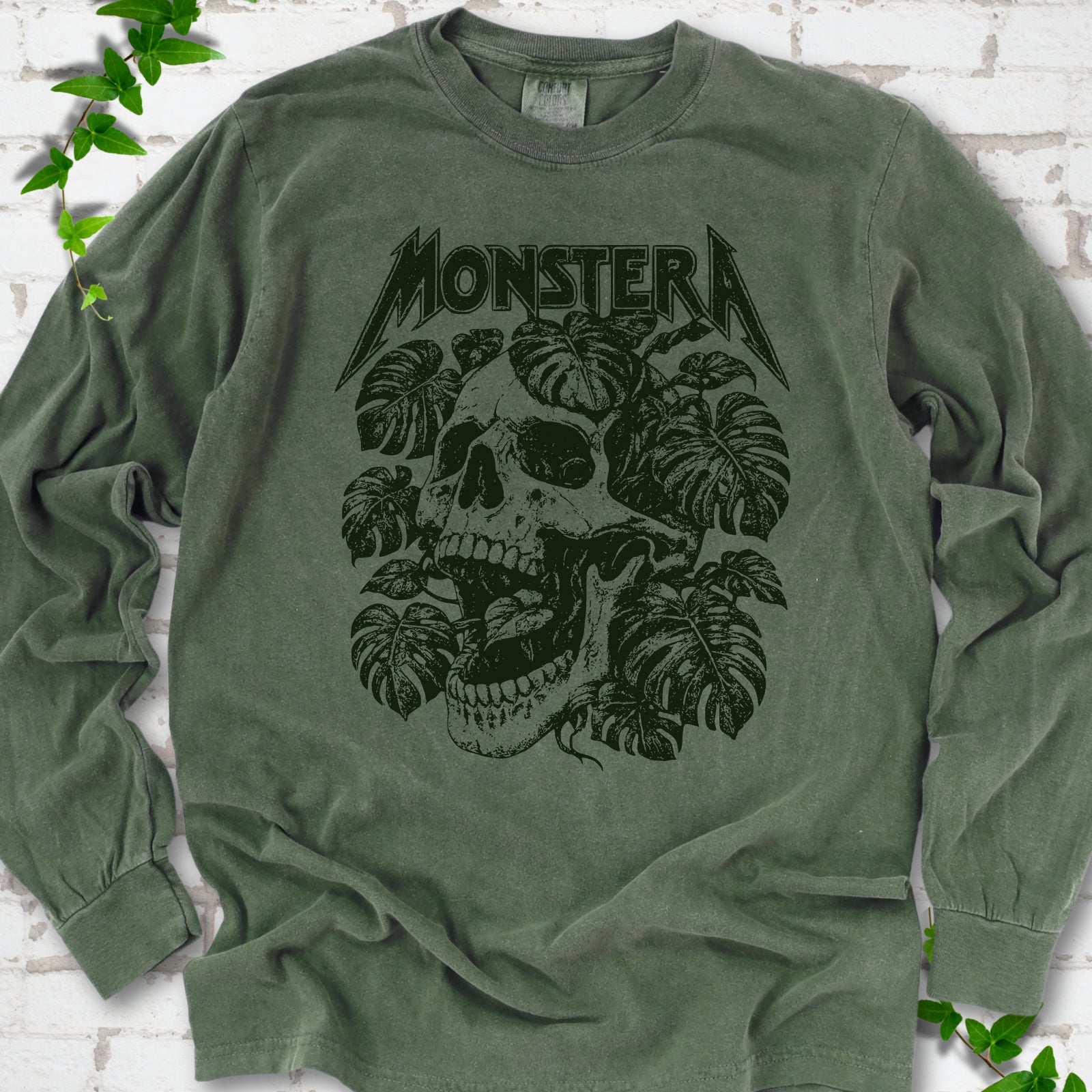 Hemp Comfort Colors® long sleeve T-shirt with distressed skull and monstera leaves beneath MONSTERA lettering, flat lay on white brick.