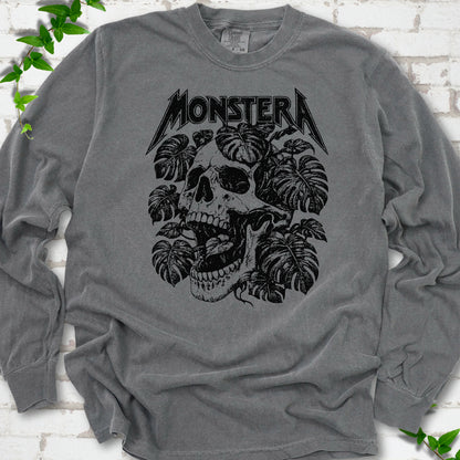 Pepper Comfort Colors® long sleeve T-shirt with distressed skull and monstera leaves beneath MONSTERA lettering, flat lay on white brick.