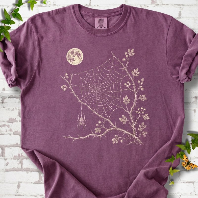 Berry Comfort Colors® T-shirt flat lay featuring a cream moon, spider web, berry branches and hanging spider design.