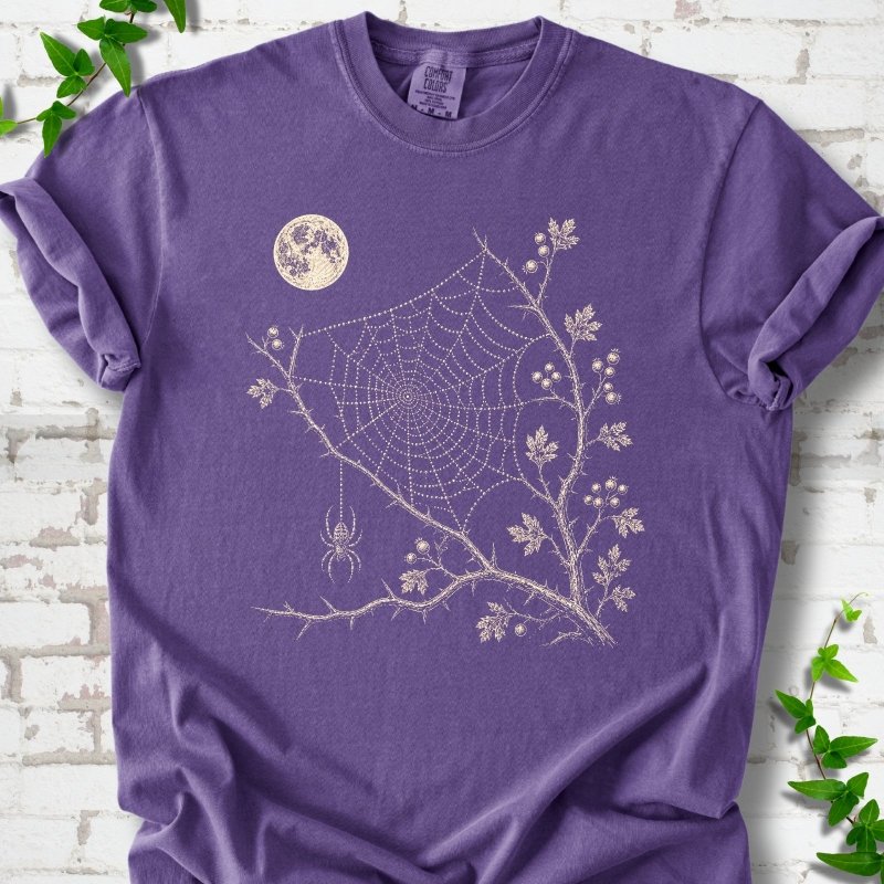 Grape Comfort Colors® T-shirt flat lay featuring a cream moon, spider web, berry branches and hanging spider design.