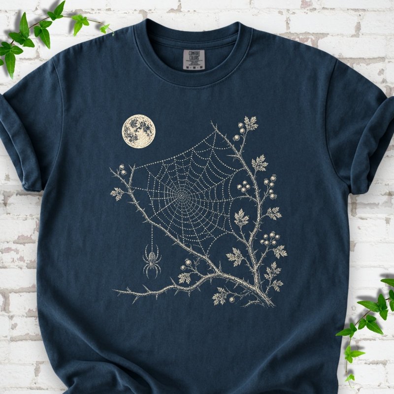 Midnight Comfort Colors® T-shirt flat lay featuring a cream moon, spider web, berry branches and hanging spider design.