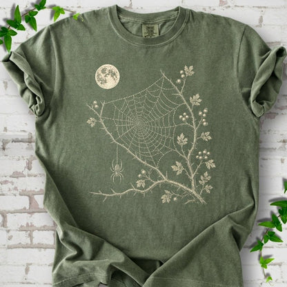 Moss Comfort Colors® T-shirt flat lay featuring a cream moon, spider web, berry branches and hanging spider design.