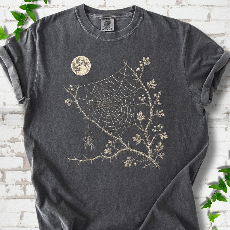 Pepper Comfort Colors® T-shirt flat lay featuring a cream moon, spider web, berry branches and hanging spider design.