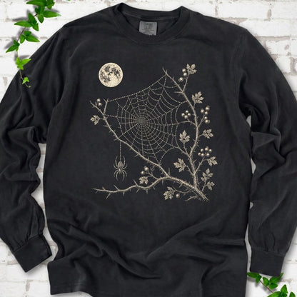 Black Comfort Colors® long sleeve T-shirt flat lay featuring a cream moon, spider web, berry branches and hanging spider design.