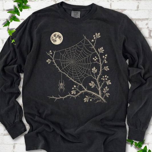 Black Comfort Colors® long sleeve T-shirt flat lay featuring a cream moon, spider web, berry branches and hanging spider design.
