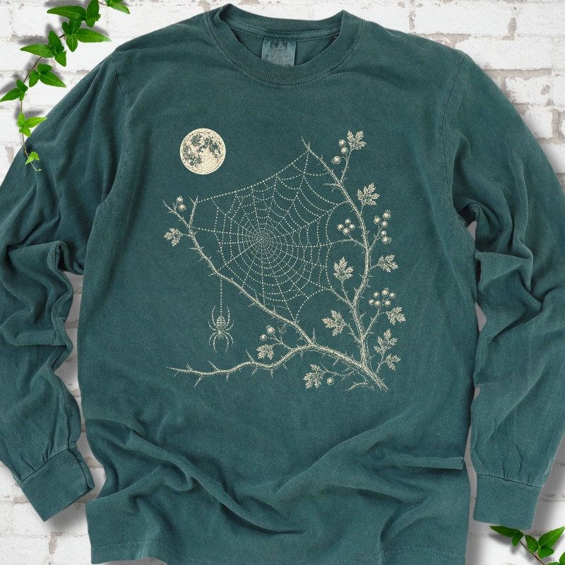 Blue Spruce Comfort Colors® long sleeve T-shirt flat lay featuring a cream moon, spider web, berry branches and hanging spider design.