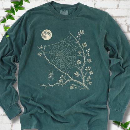 Blue Spruce Comfort Colors® long sleeve T-shirt flat lay featuring a cream moon, spider web, berry branches and hanging spider design.