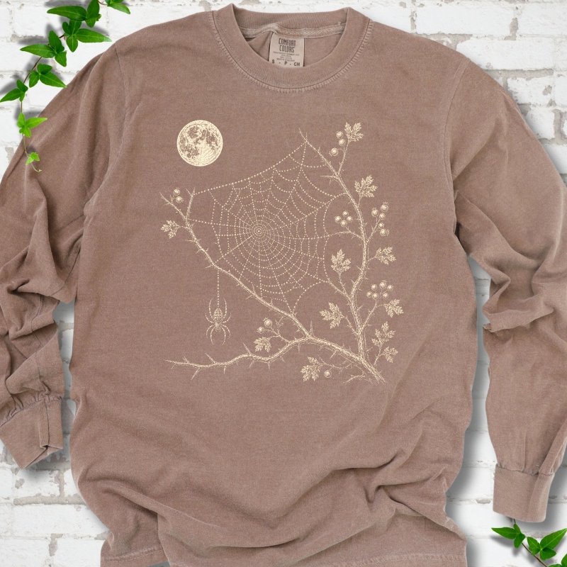 Espresso Comfort Colors® long sleeve T-shirt flat lay featuring a cream moon, spider web, berry branches and hanging spider design.