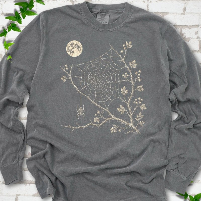 Pepper Comfort Colors® long sleeve T-shirt flat lay featuring a cream moon, spider web, berry branches and hanging spider design.