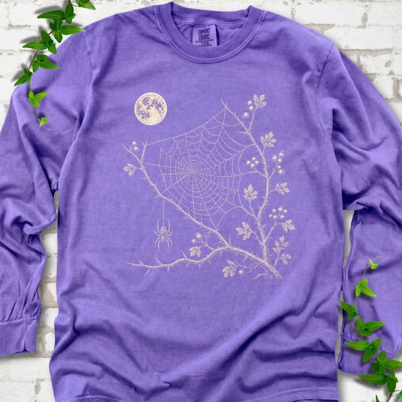 Violet Comfort Colors® long sleeve T-shirt flat lay featuring a cream moon, spider web, berry branches and hanging spider design.