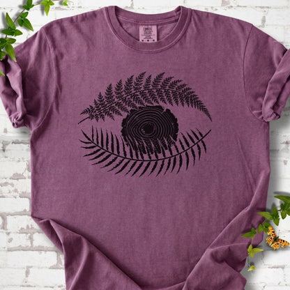 Berry Comfort Colors® T-shirt flat lay featuring a black botanical eye formed by fern fronds and a tree-ring centre.