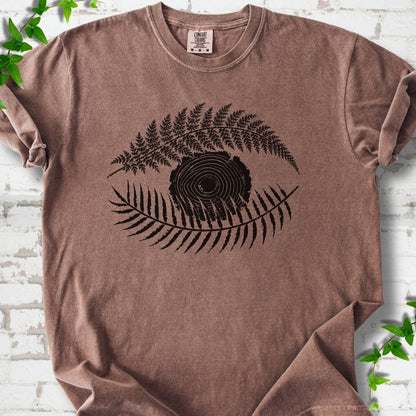 Espresso Comfort Colors® T-shirt flat lay featuring a black botanical eye formed by fern fronds and a tree-ring centre.