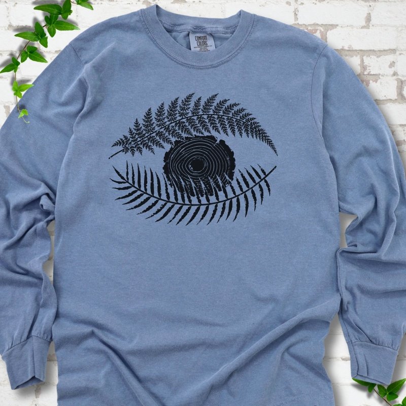 Blue Jean Comfort Colors® long sleeve T-shirt flat lay featuring a black botanical eye formed by fern fronds and a tree-ring centre.