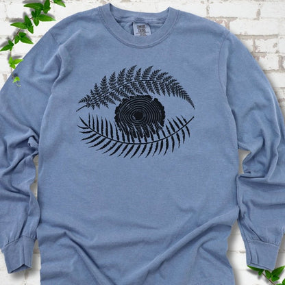 Blue Jean Comfort Colors® long sleeve T-shirt flat lay featuring a black botanical eye formed by fern fronds and a tree-ring centre.