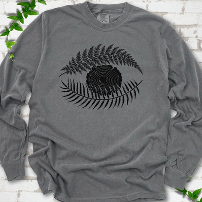 Pepper Comfort Colors® long sleeve T-shirt flat lay featuring a black botanical eye formed by fern fronds and a tree-ring centre.