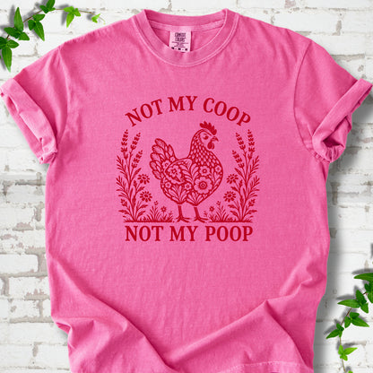Crunchberry T-shirt flat lay with a bright red folk-art hen surrounded by wildflowers and lavender, "Not my coop" arched above and "Not my poop" below, on white brick with ivy.