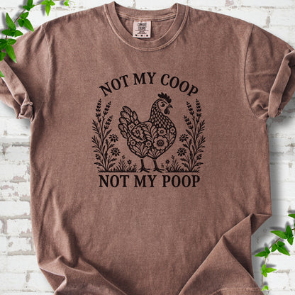 Espresso T-shirt flat lay with a dark brown folk-art hen surrounded by wildflowers and lavender, "Not my coop" arched above and "Not my poop" below, on white brick with ivy.