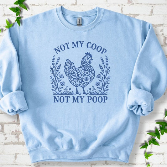 Light Blue sweatshirt flat lay with a mid blue folk-art hen surrounded by wildflowers and lavender, "Not my coop" arched above and "Not my poop" below, on white brick with ivy.