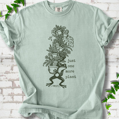 Bay Comfort Colors® T-shirt flat lay featuring a frog carrying a tall stack of houseplants and the words just one more plant.