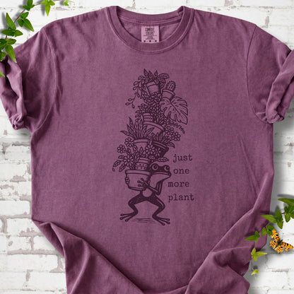 Berry Comfort Colors® T-shirt flat lay featuring a frog carrying a tall stack of houseplants and the words just one more plant.