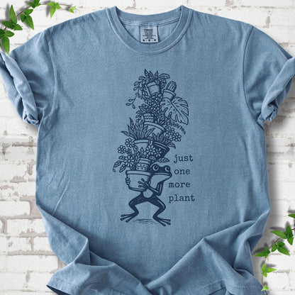 Blue Jean Comfort Colors® T-shirt flat lay featuring a frog carrying a tall stack of houseplants and the words just one more plant.