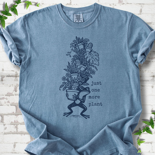 Blue Jean Comfort Colors® T-shirt flat lay featuring a frog carrying a tall stack of houseplants and the words just one more plant.