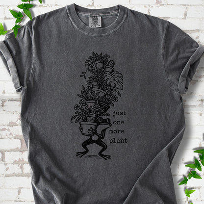 Pepper Comfort Colors® T-shirt flat lay featuring a frog carrying a tall stack of houseplants and the words just one more plant.