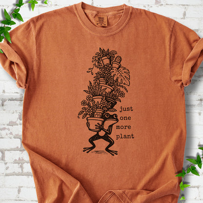 Yam Comfort Colors® T-shirt flat lay featuring a frog carrying a tall stack of houseplants and the words just one more plant.