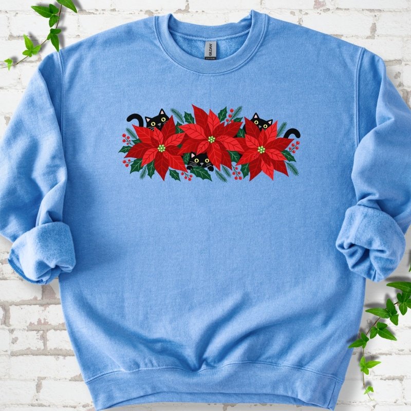 Carolina Blue classic sweatshirt shown flat with black cats peeking through red poinsettias and holiday greenery