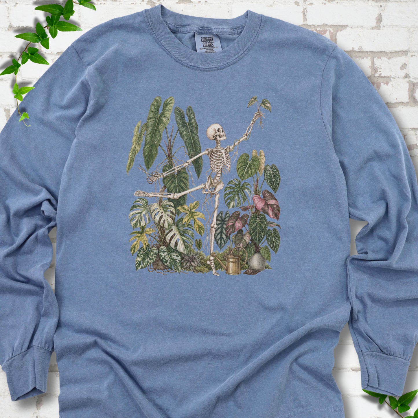 Blue Jean Comfort Colors® long sleeve T-shirt front mockup featuring a skeleton tending a collection of leafy houseplants.