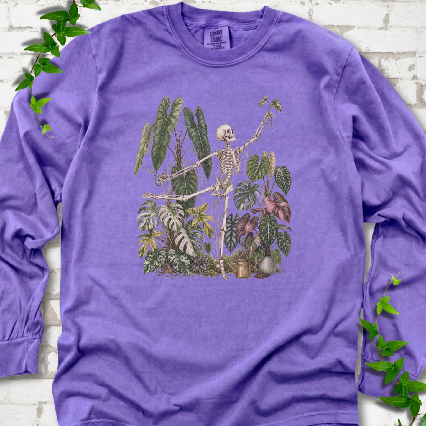 Violet Comfort Colors® long sleeve T-shirt front mockup featuring a skeleton tending a collection of leafy houseplants.
