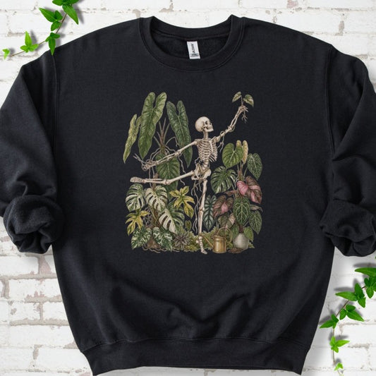 Black Gildan® 18000 crewneck sweatshirt flat lay featuring a skeleton tending a collection of tropical houseplants.
