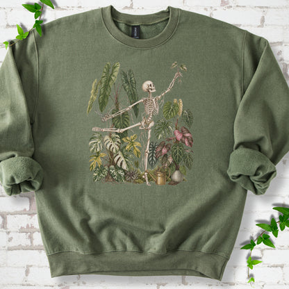 Military Green Gildan® 18000 crewneck sweatshirt flat lay featuring a skeleton tending a collection of tropical houseplants.