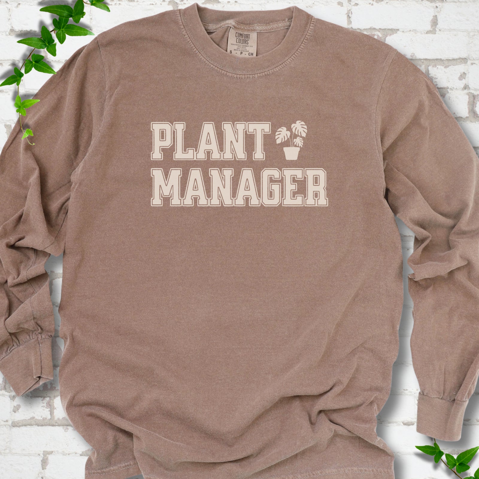 Espresso Comfort Colors® long sleeve T-shirt front mockup featuring the collegiate Plant Manager design with a potted monstera.