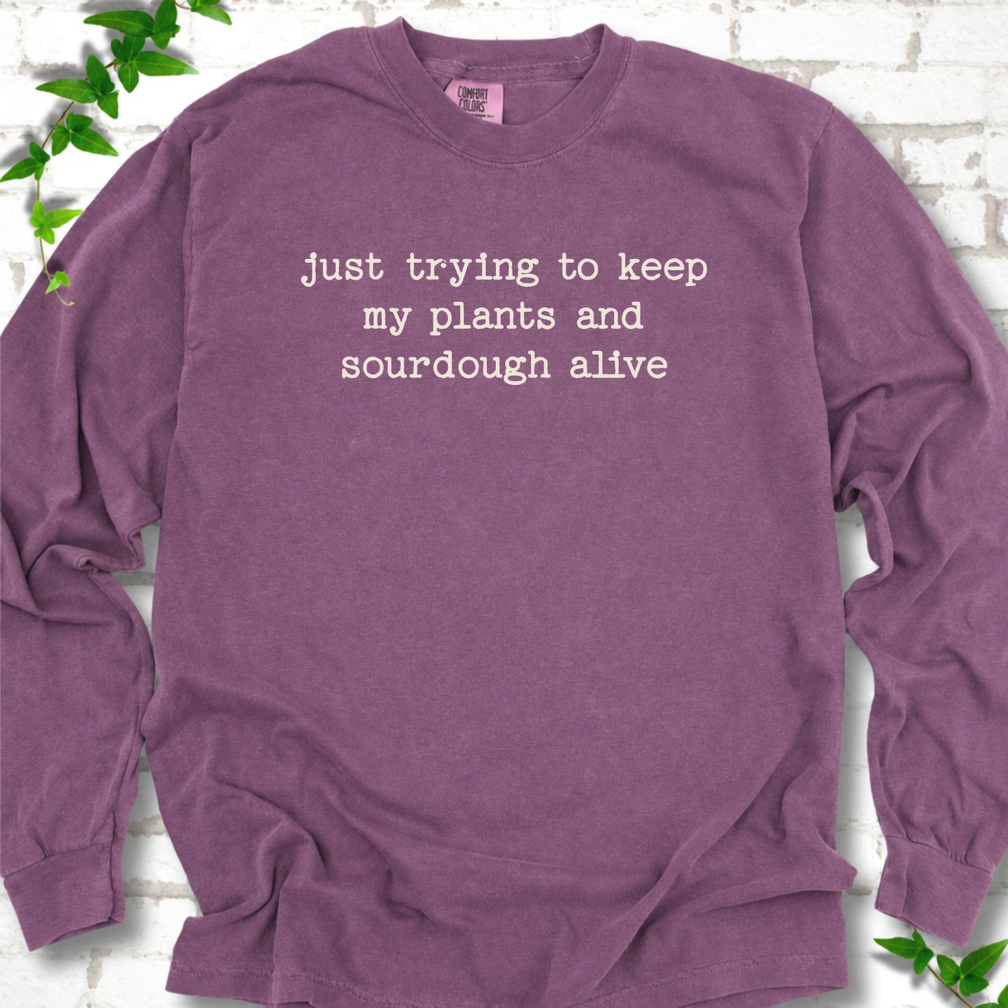 Berry Comfort Colors® long sleeve T-shirt front mockup featuring the words “just trying to keep my plants and sourdough alive.”