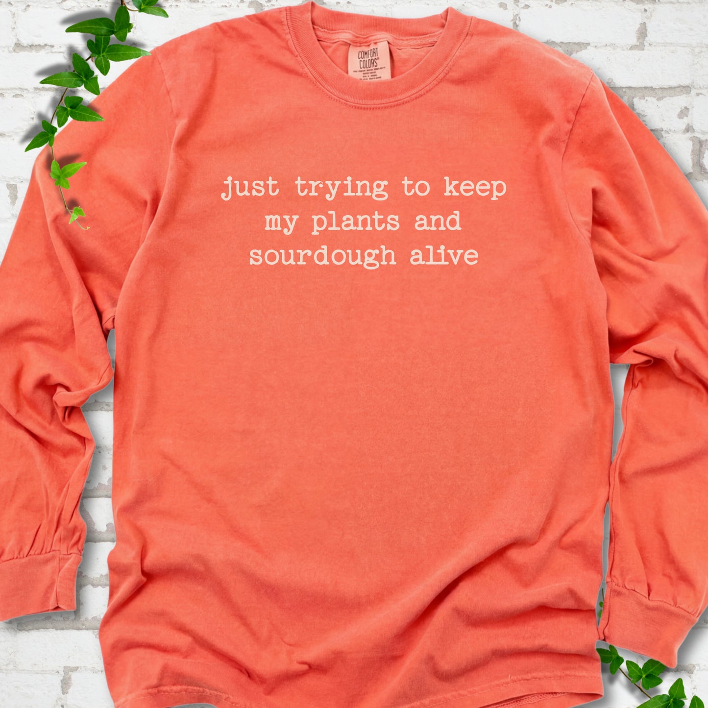 Bright Salmon Comfort Colors® long sleeve T-shirt front mockup featuring the words “just trying to keep my plants and sourdough alive.”