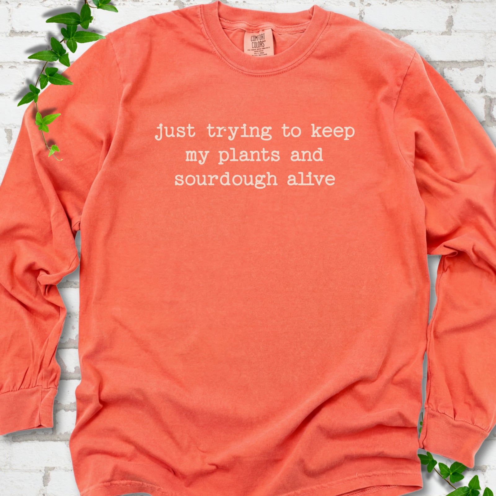 Bright Salmon Comfort Colors® long sleeve T-shirt front mockup featuring the words “just trying to keep my plants and sourdough alive.”
