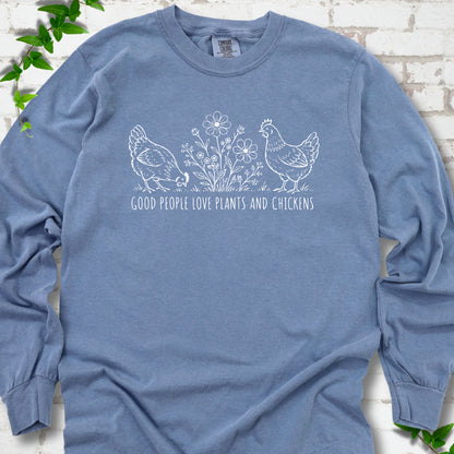 Blue Jean long-sleeve T-shirt flat lay with white line-art hens and flowers above the words "Good People Love Plants and Chickens."