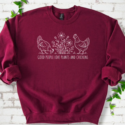 Maroon crewneck sweatshirt flat lay with white line-art hens and flowers above the words "Good People Love Plants and Chickens."