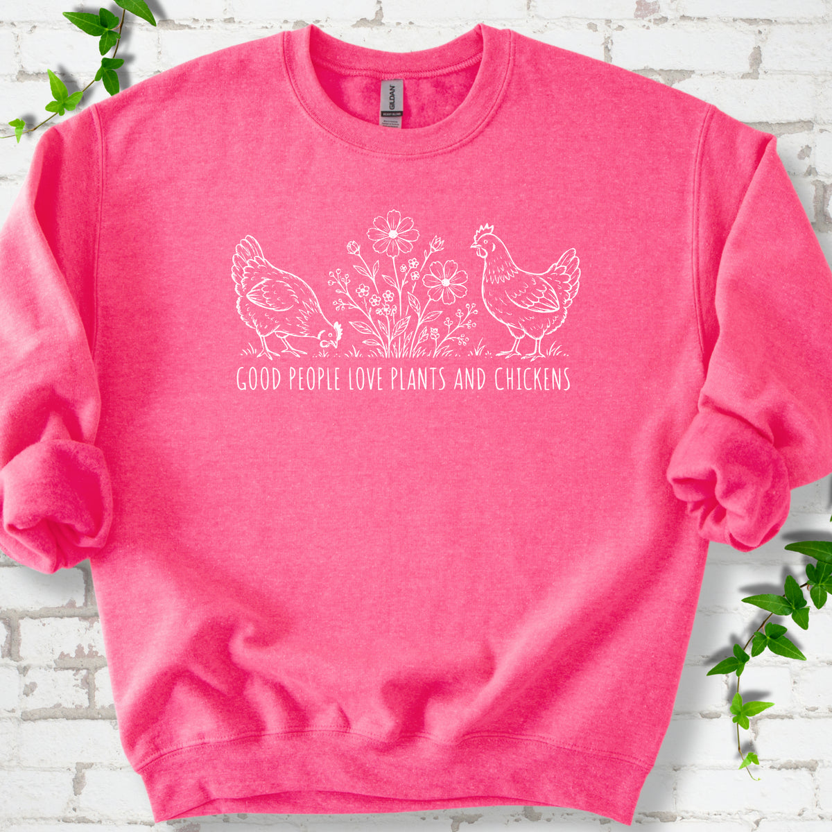 Safety Pink crewneck sweatshirt flat lay with white line-art hens and flowers above the words "Good People Love Plants and Chickens."