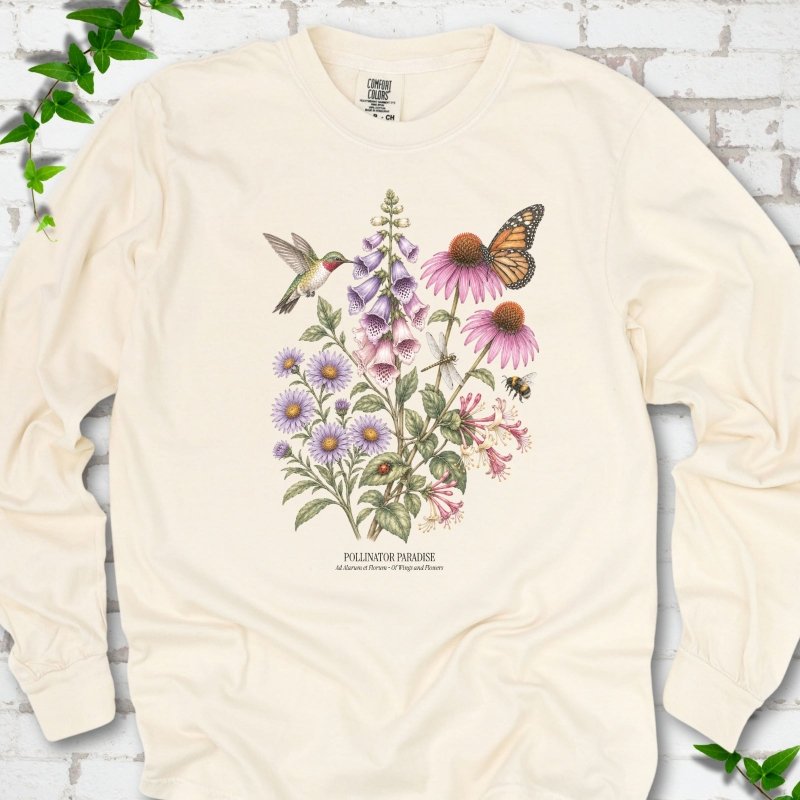 Ivory Comfort Colors® long sleeve T-shirt flat lay featuring a hummingbird, monarch butterfly and bee among foxglove, coneflowers and asters with Pollinator Paradise text.