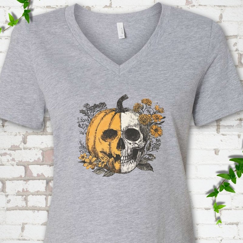Athletic Heather Bella Canvas® ladies' V-neck T-shirt flat lay featuring a half-pumpkin, half-skull botanical Halloween graphic.