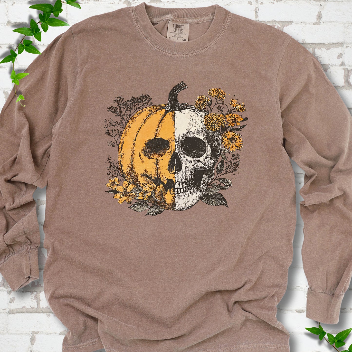 Espresso Comfort Colors® long sleeve T-shirt flat lay featuring a half-pumpkin, half-skull botanical Halloween graphic.