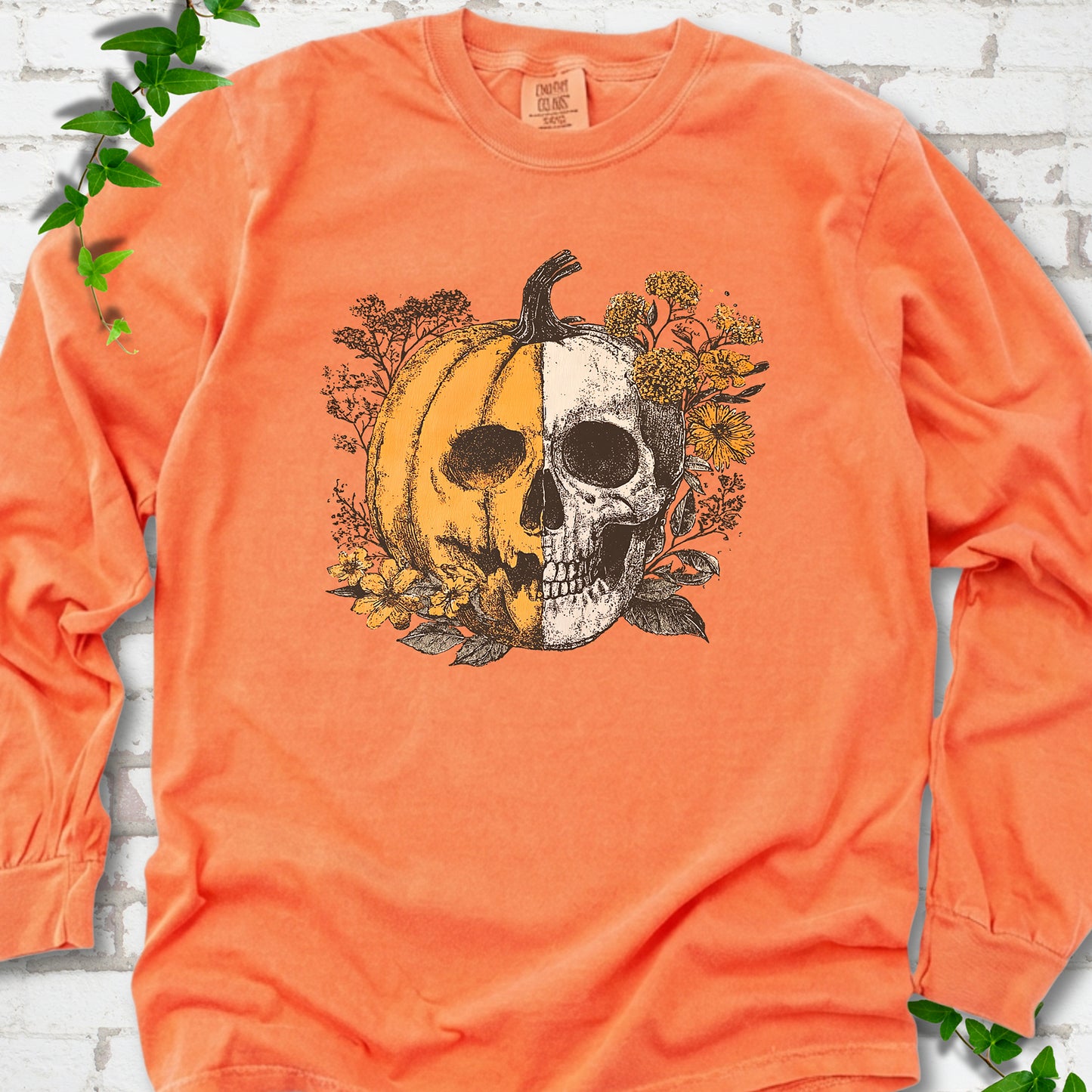 Melon Comfort Colors® long sleeve T-shirt flat lay featuring a half-pumpkin, half-skull botanical Halloween graphic.