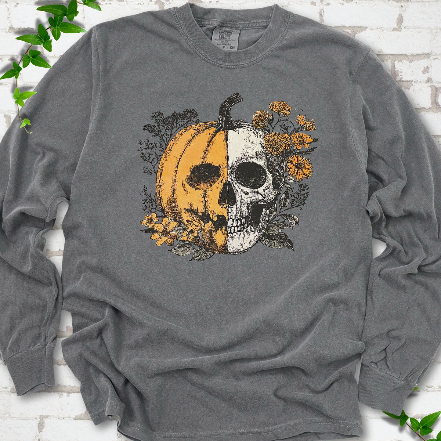 Pepper Comfort Colors® long sleeve T-shirt flat lay featuring a half-pumpkin, half-skull botanical Halloween graphic.